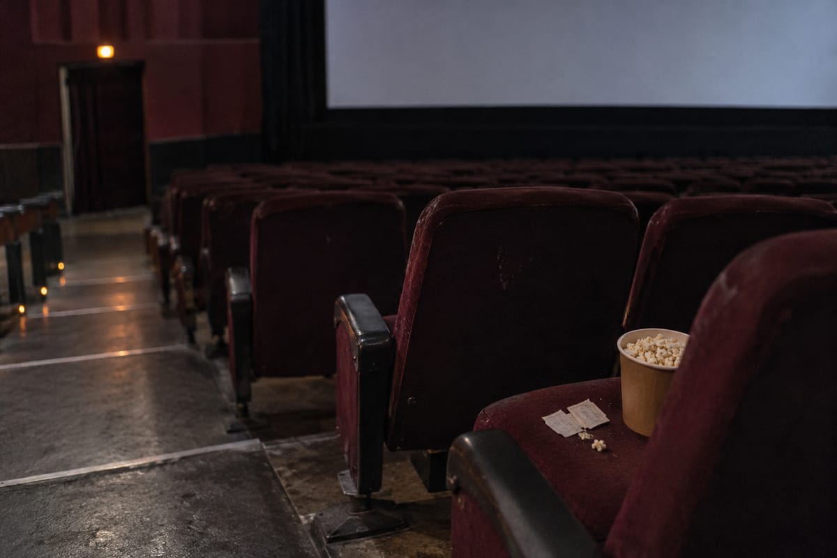 Representational AI illustration of an empty cinema with burgundy seats, popcorn and a blank screen.